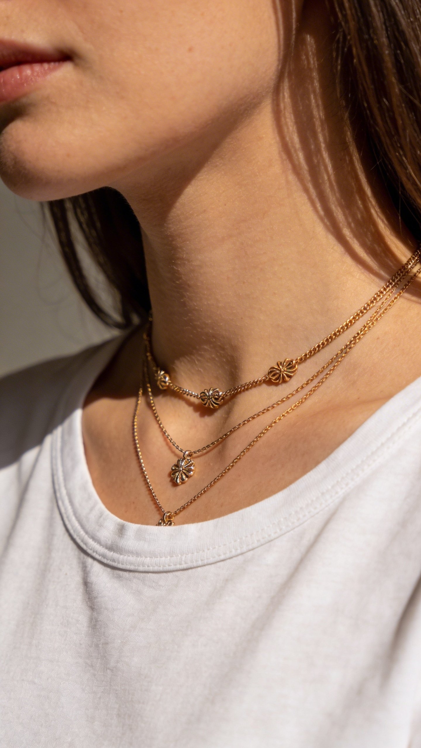 Woman's neck wearing layered delicate gold necklaces, white tee