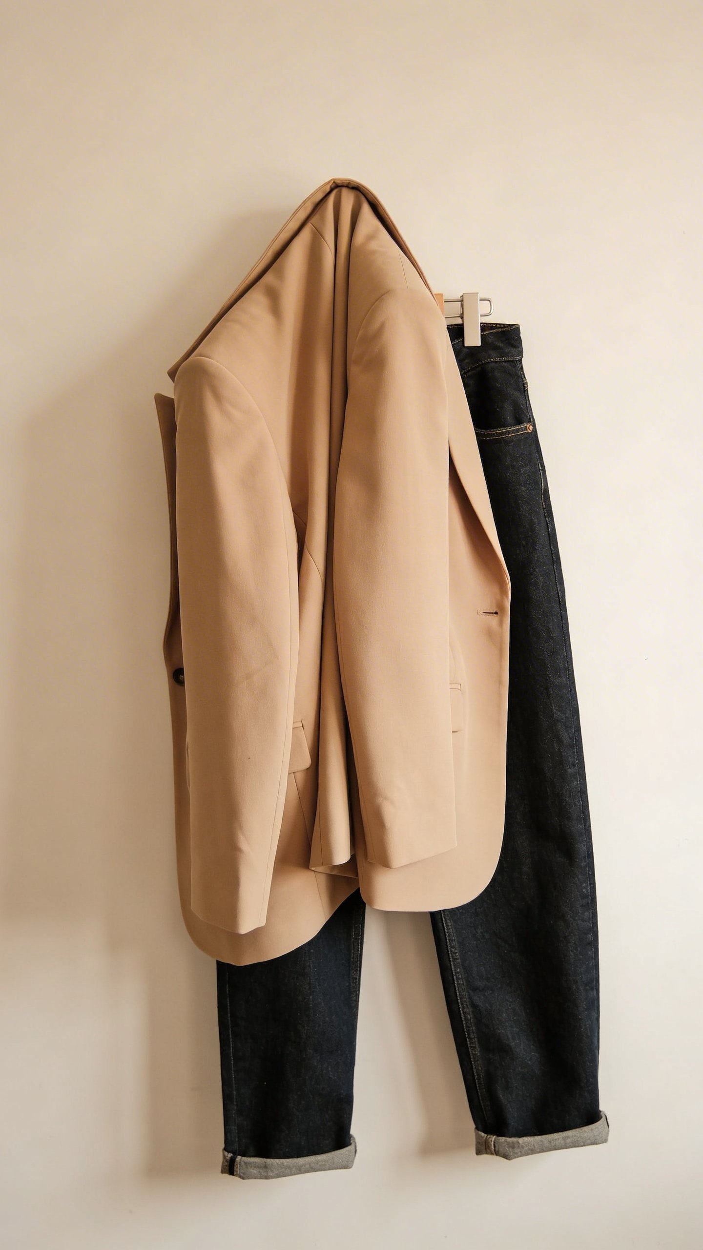 Beige structured blazer draped over dark denim jeans