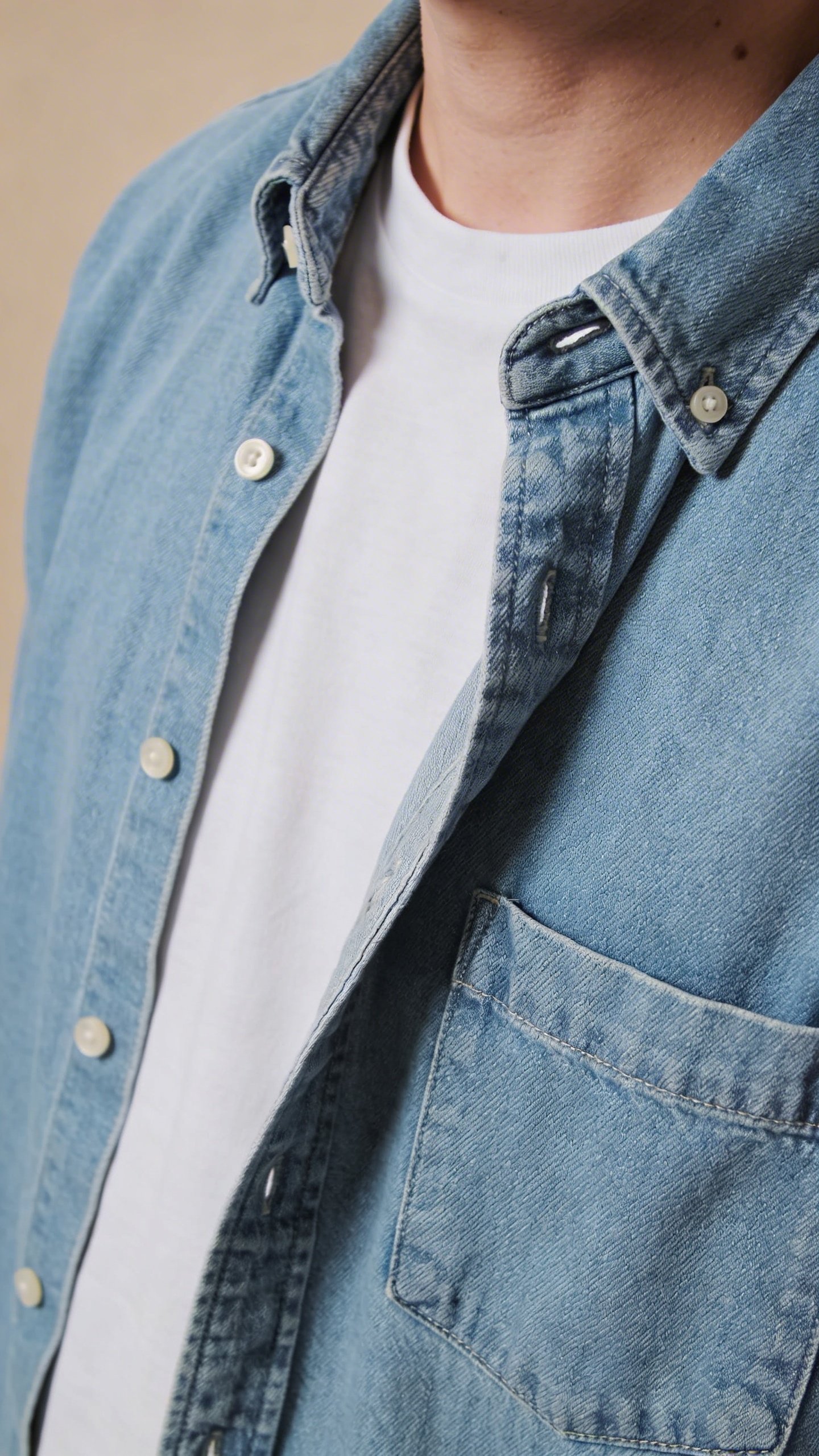 Closeup of light blue denim shirt unbuttoned over white tee