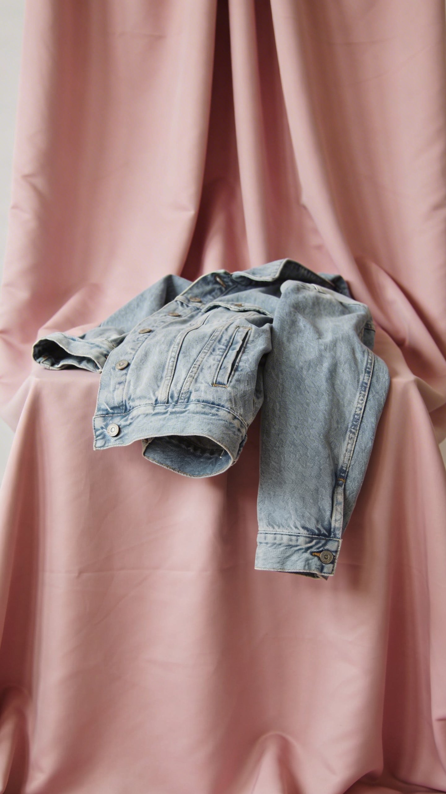 Light denim jacket draped over blush pink fabric