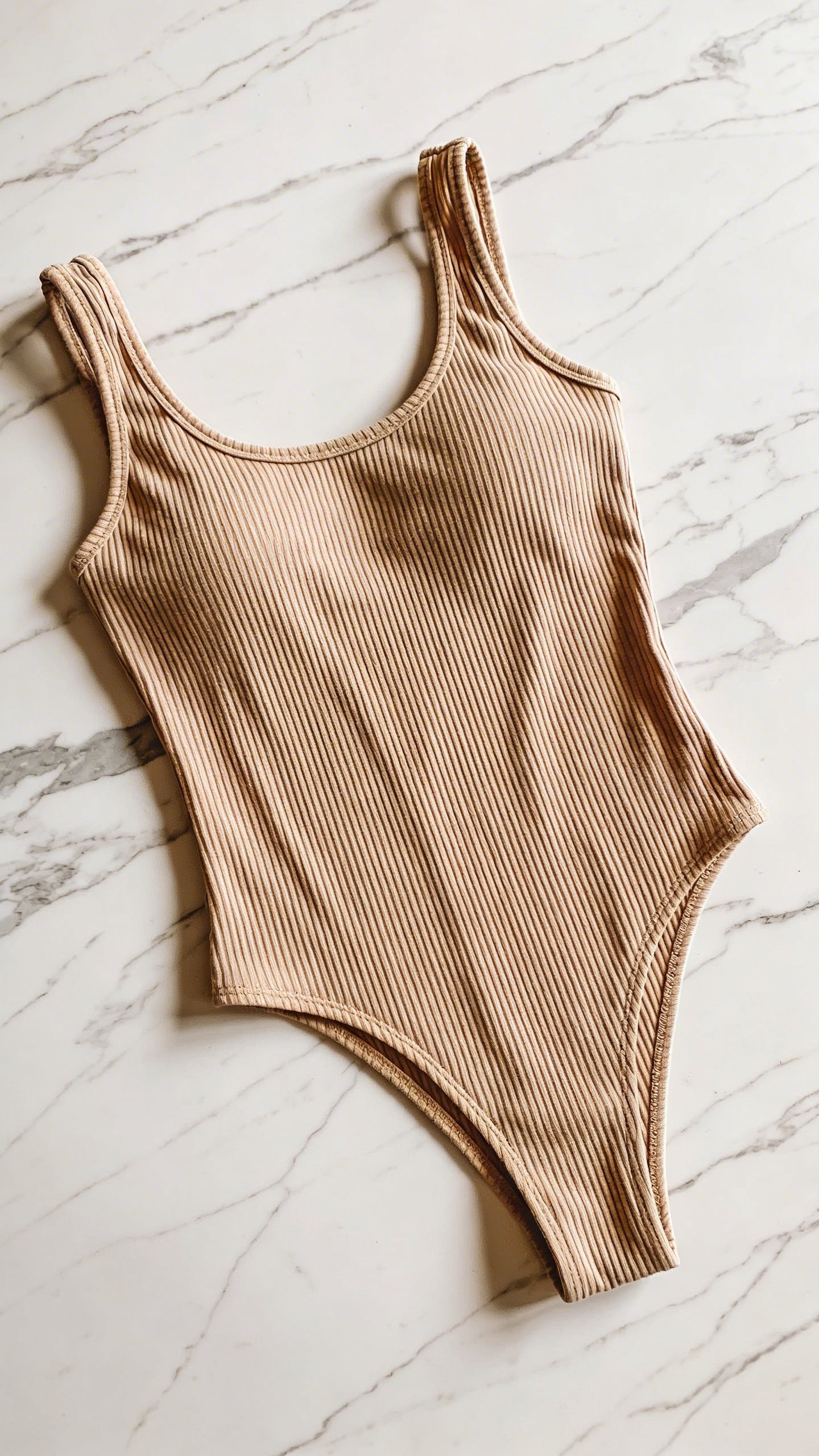 Beige ribbed knit bodysuit flatlay on marble surface