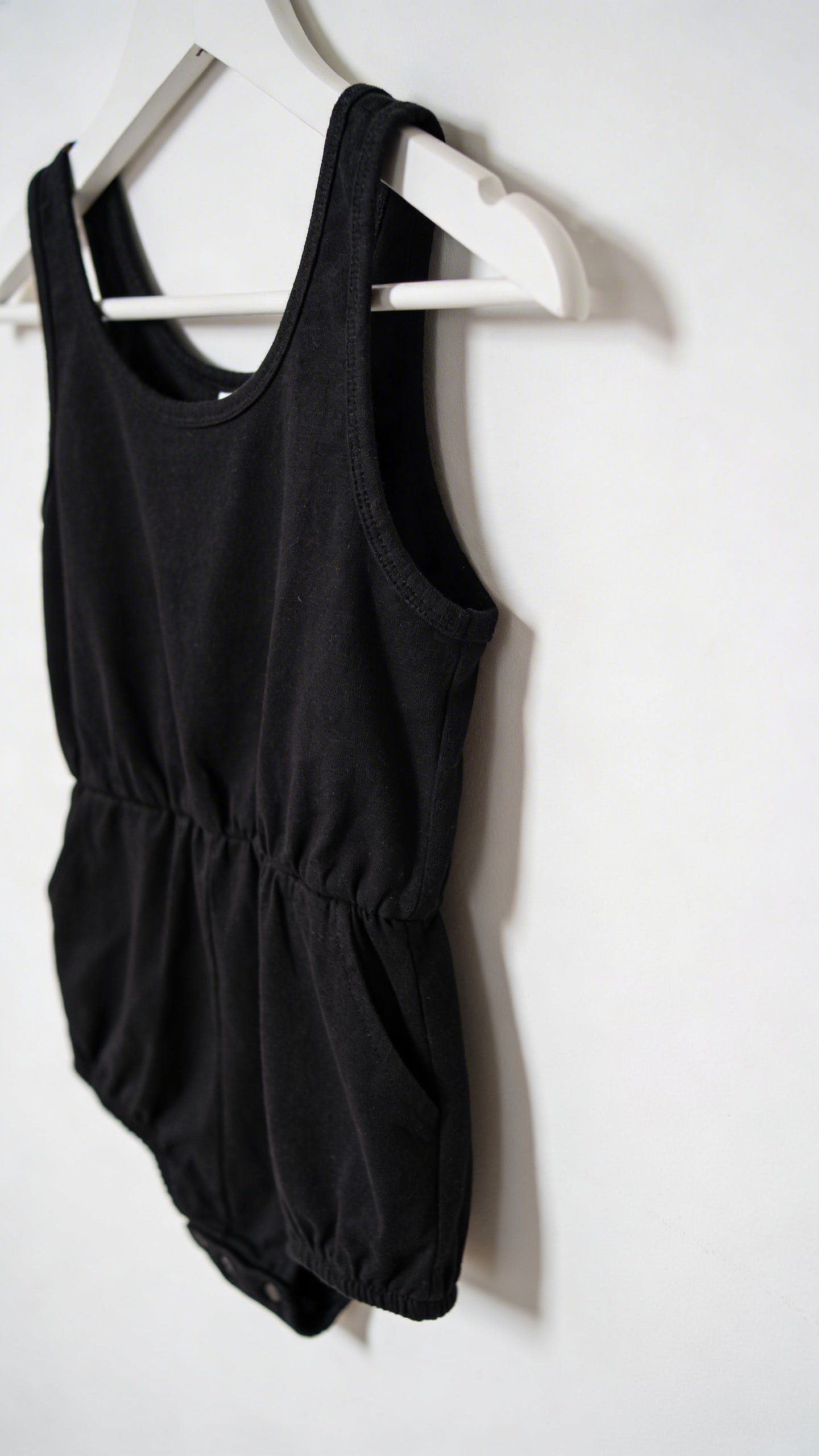 Closeup of black cotton romper on white hanger