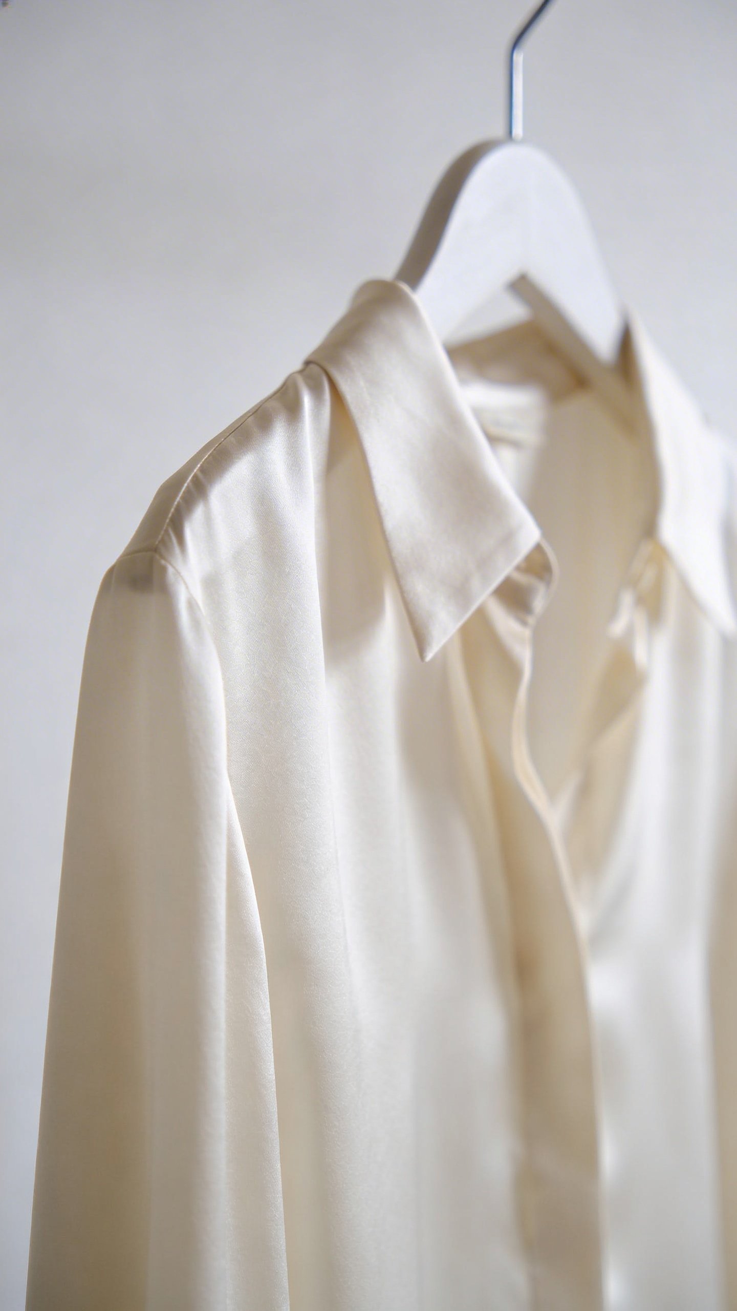 Silk ivory blouse hanging against minimal background