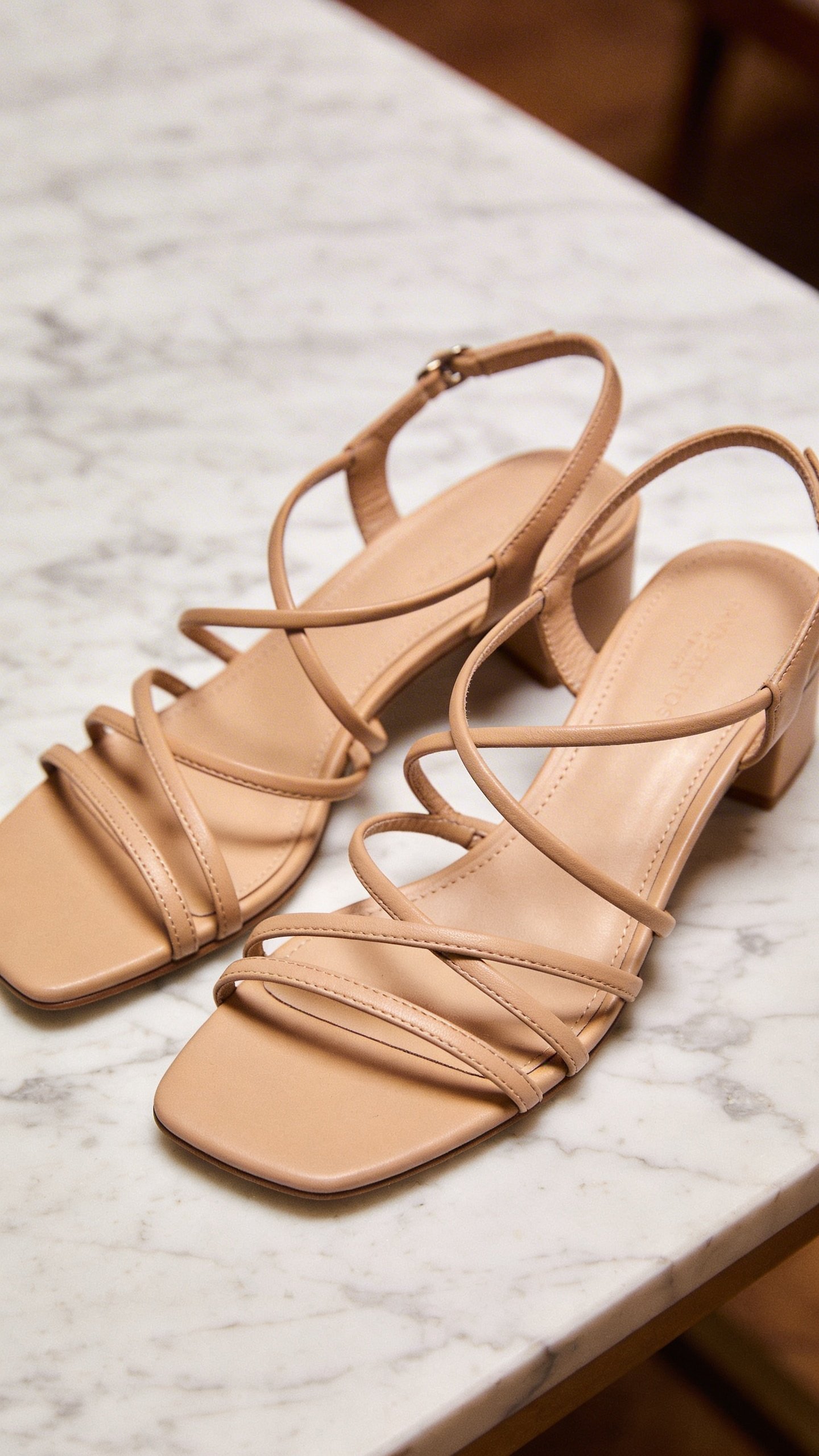 Pair of strappy beige sandals on marble surface