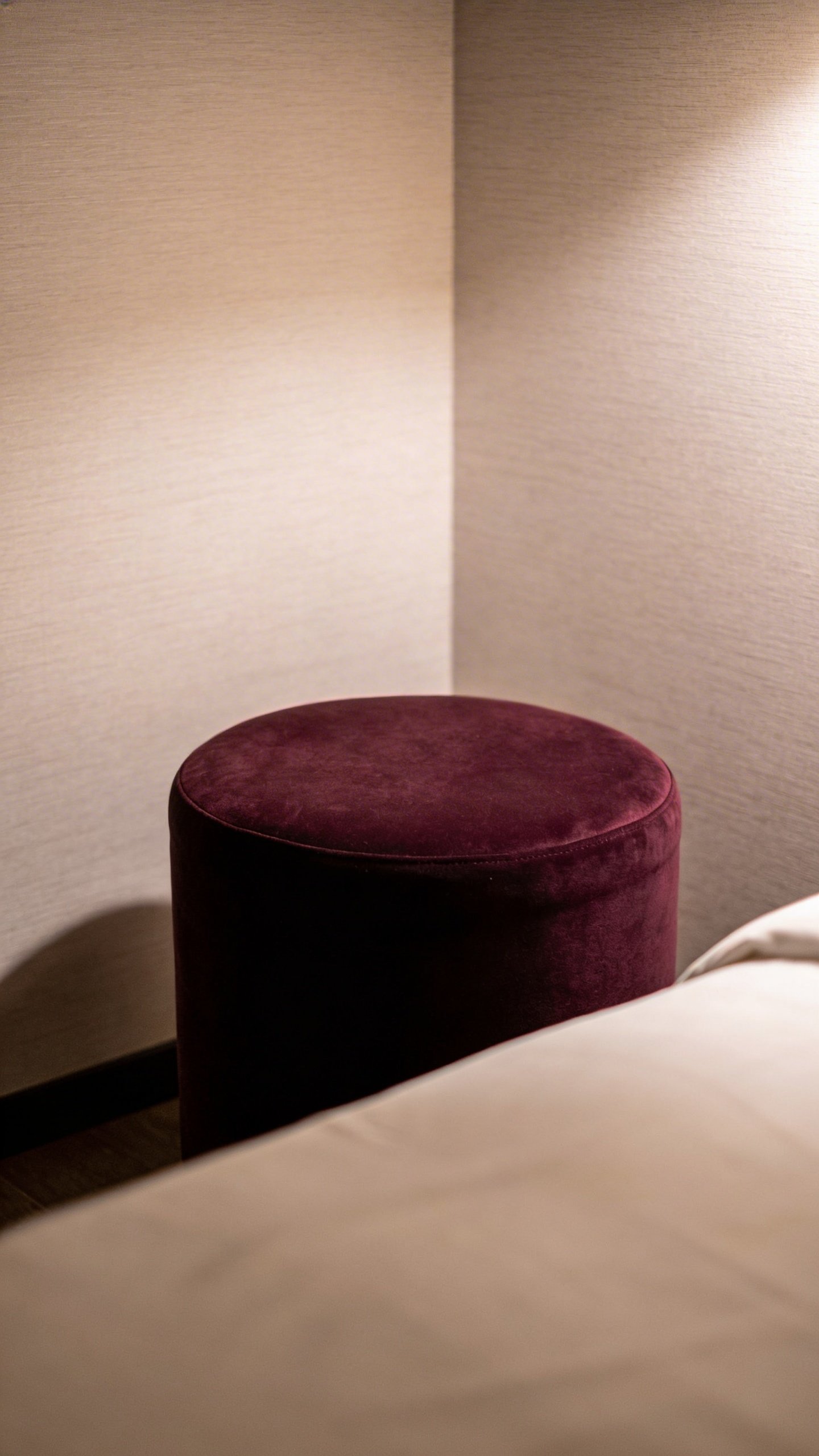 Round velvet ottoman positioned in empty bedroom corner