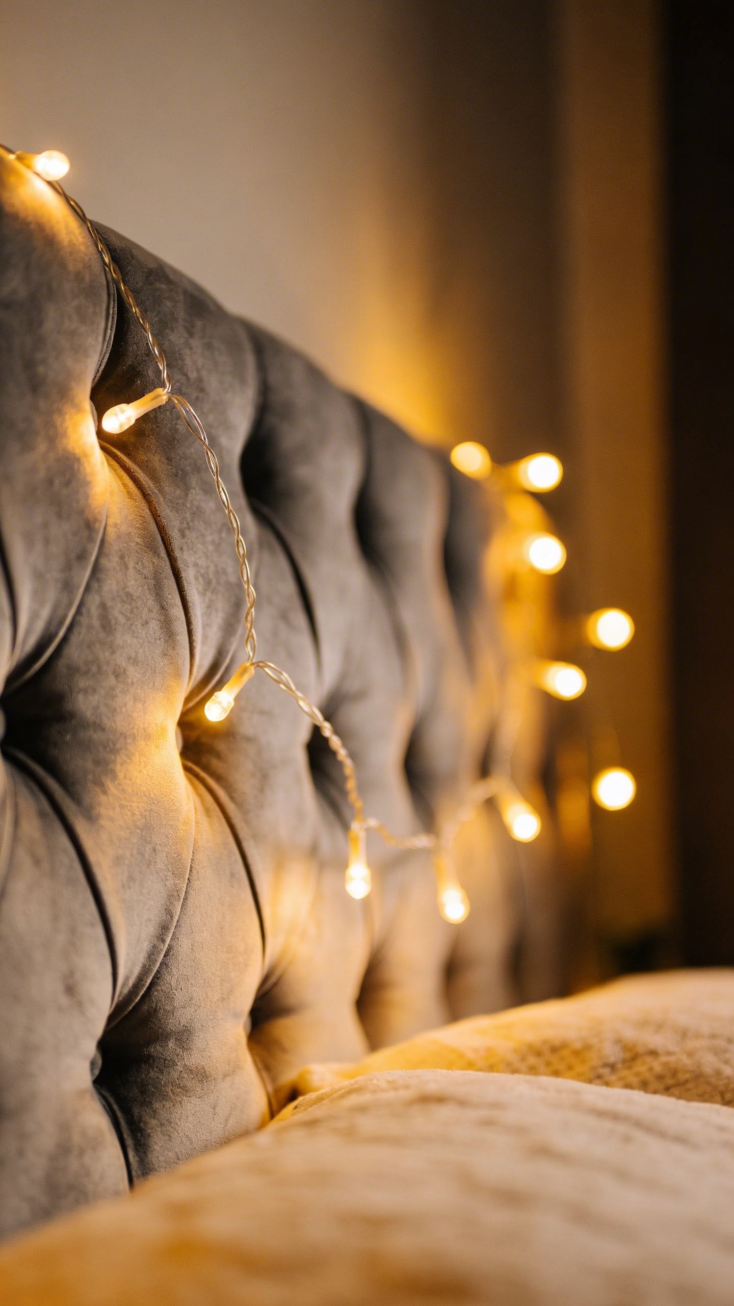 Warm string lights draped on gray upholstered headboard