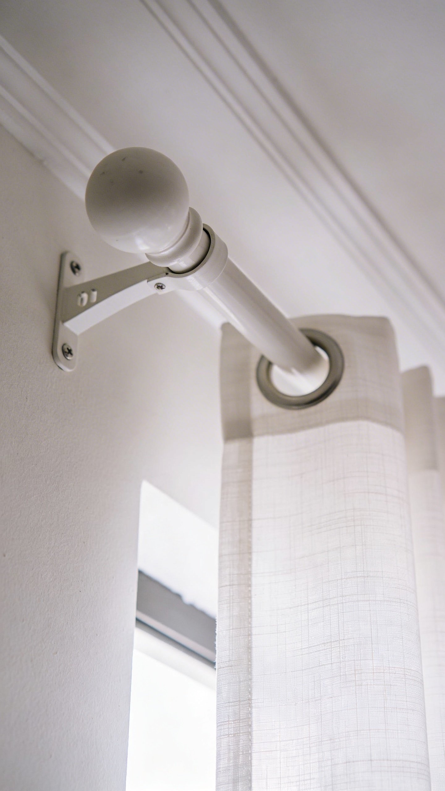 Closeup of white curtain rod mounted near ceiling