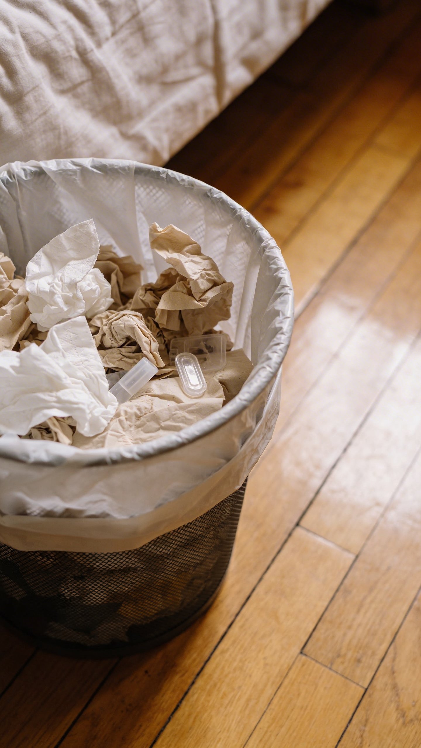 Closeup of overflowing bedroom trash bag on hardwood floor