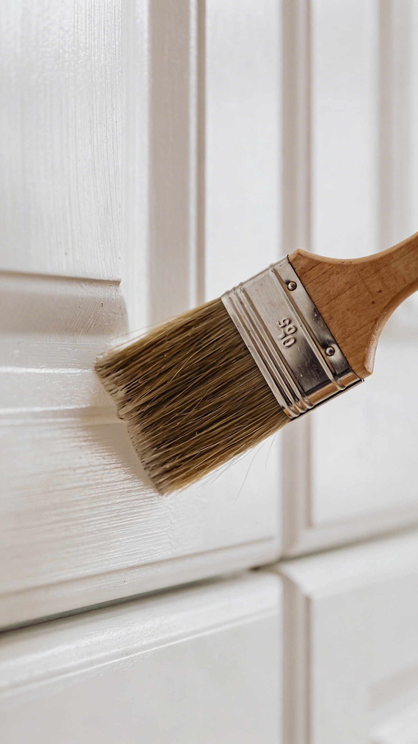 Closeup of paintbrush on white kitchen cabinet door