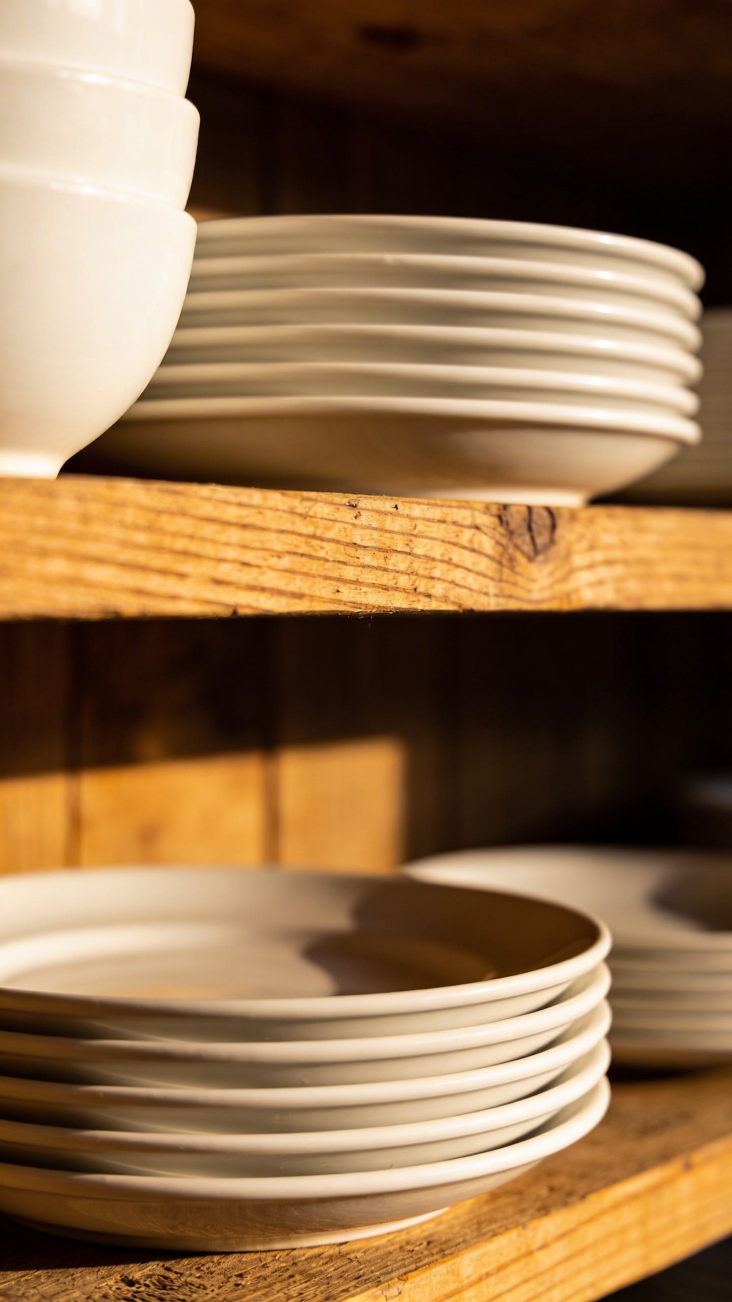 Closeup of white ceramic dishes stacked on wooden shelf
