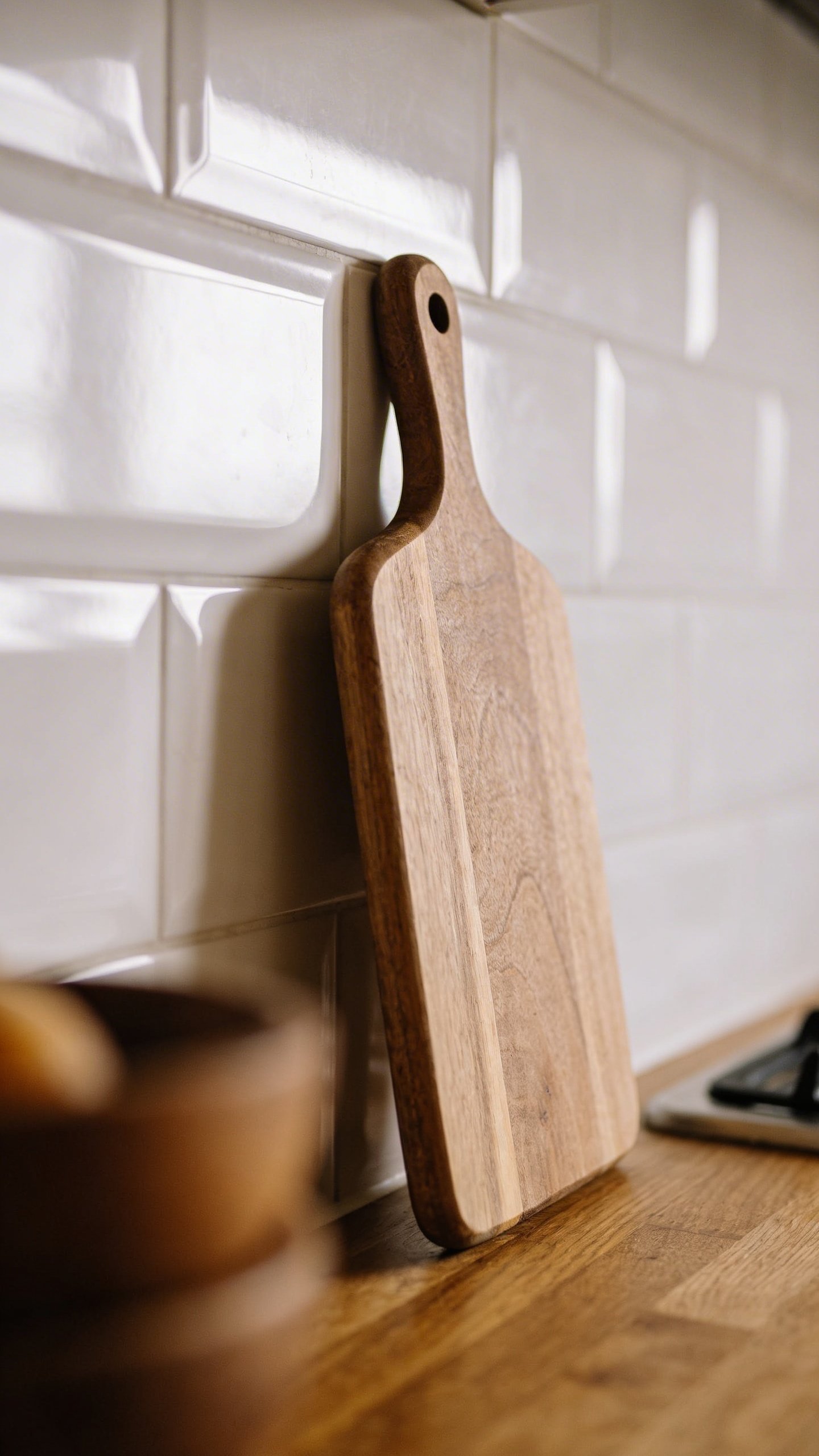Single wooden cutting board leaning against white backsplash