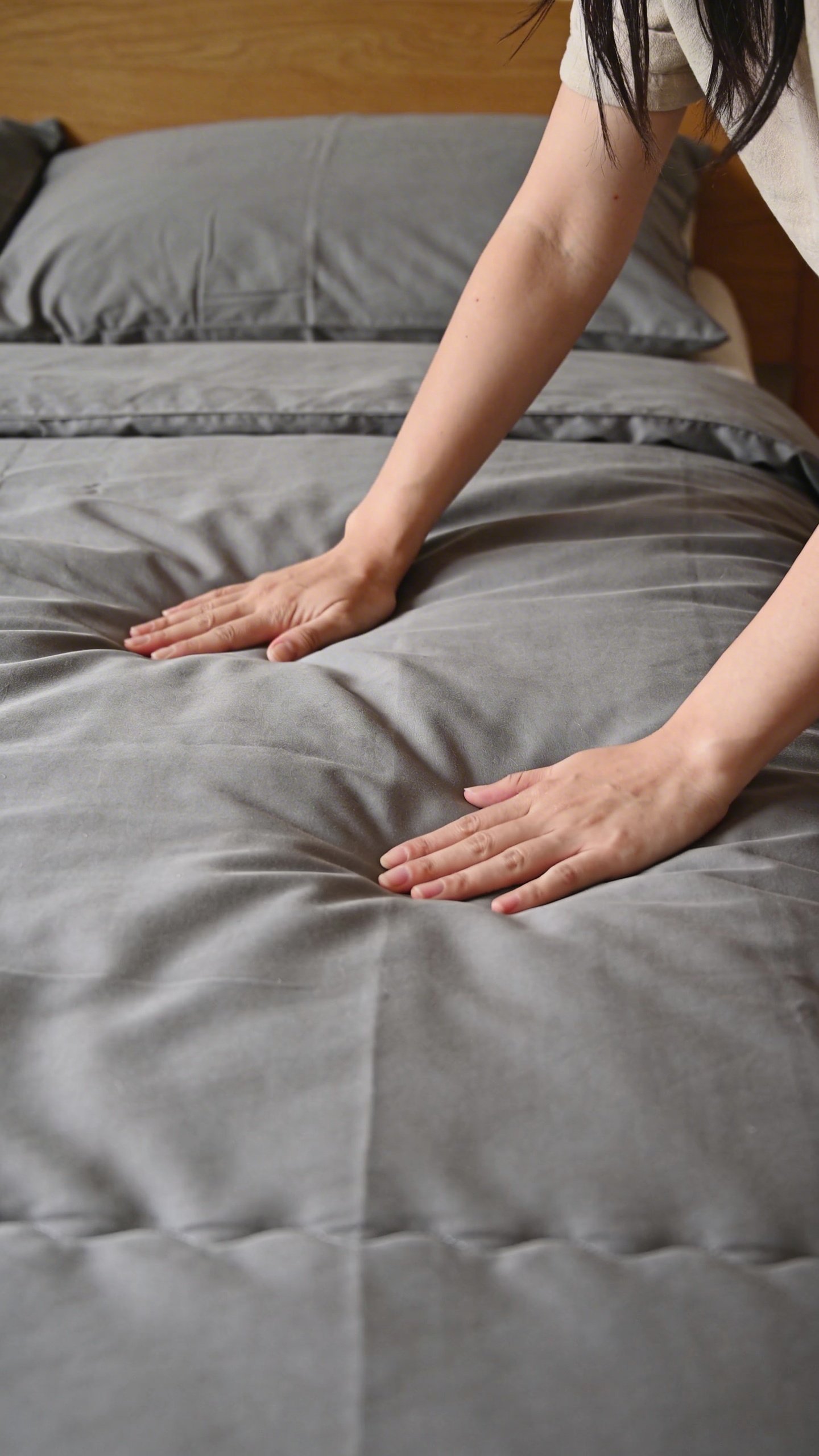 Woman's hands smoothing down gray duvet cover on bed